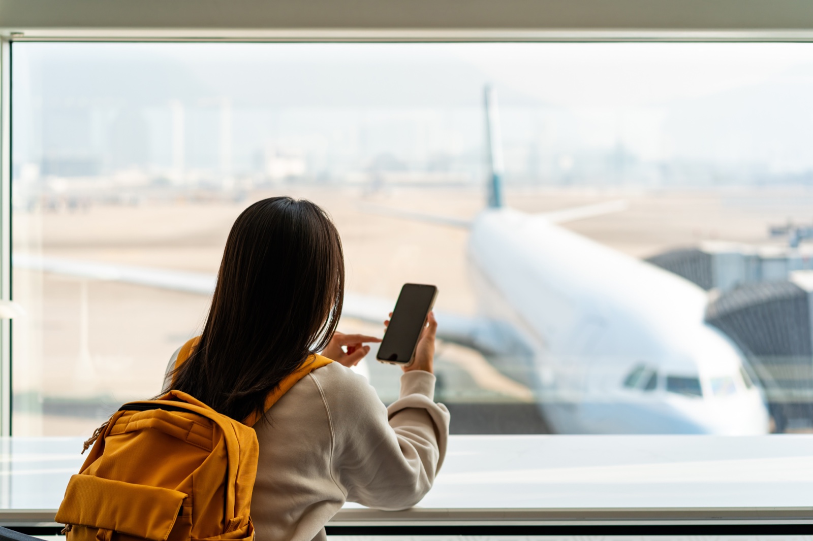 공항 라운지 통유리 앞에서 여객기를 바라보는 배낭 멘 뒷모습